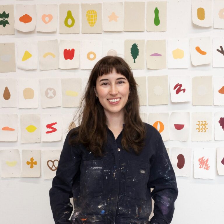 Megan Arne stands proudly in front of a series of small prints of her abstract artwork.