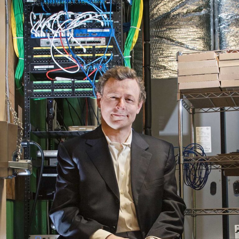STH professor Wesley Wildman poses alongside high-powered computing technology to study religious questions. Photo by Jackie Ricciardi for Boston University.