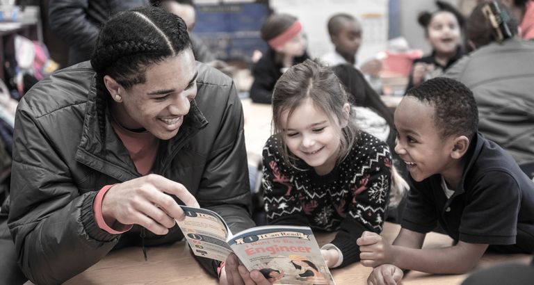 Student reading to small children at a table in Boston Public Schools