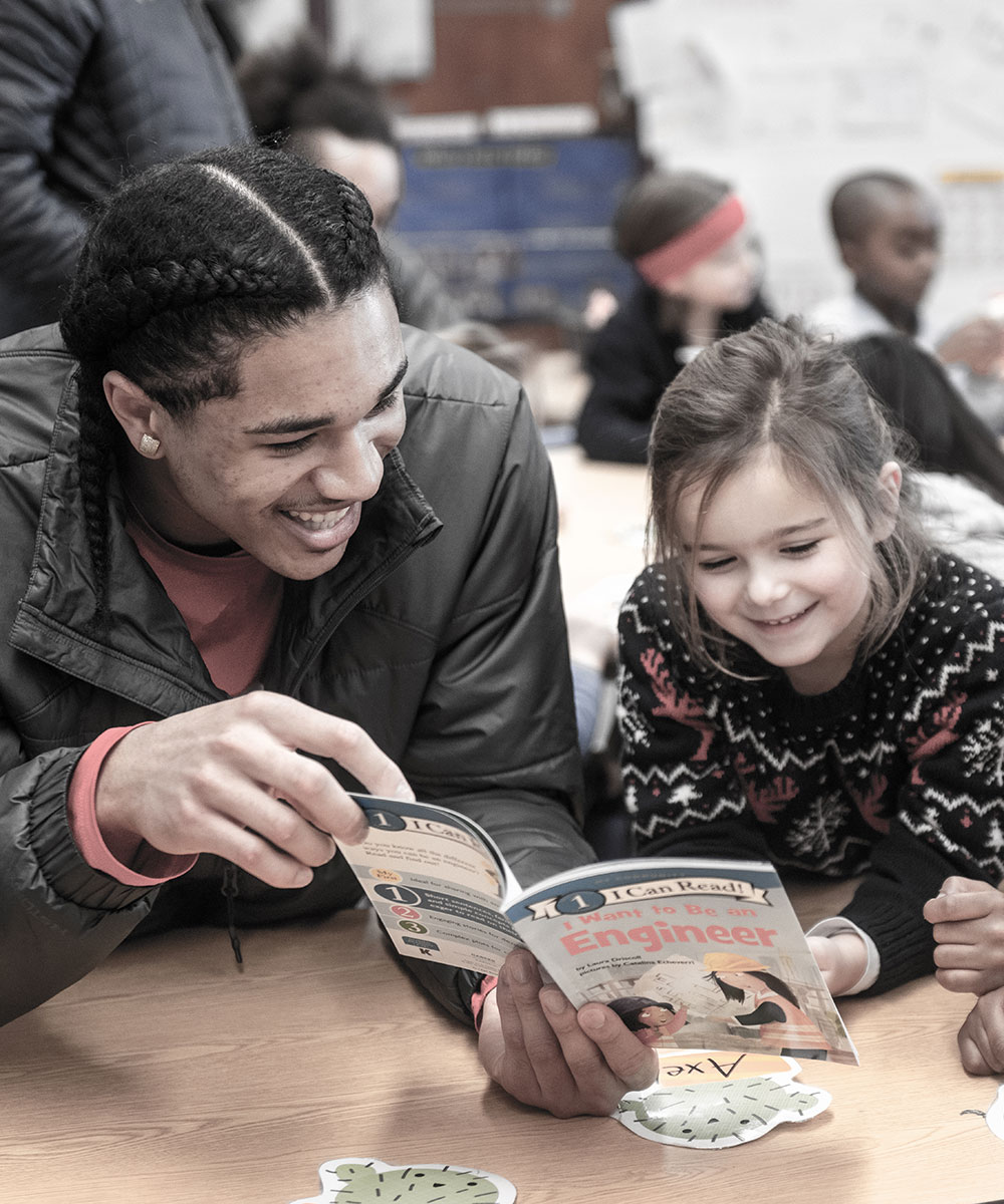 Student reading to small children at a table in Boston Public Schools