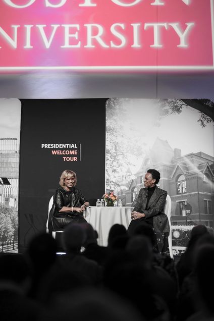 President Melissa Gilliam sitting at a table on stage with another woman with a crowd of people in front of them